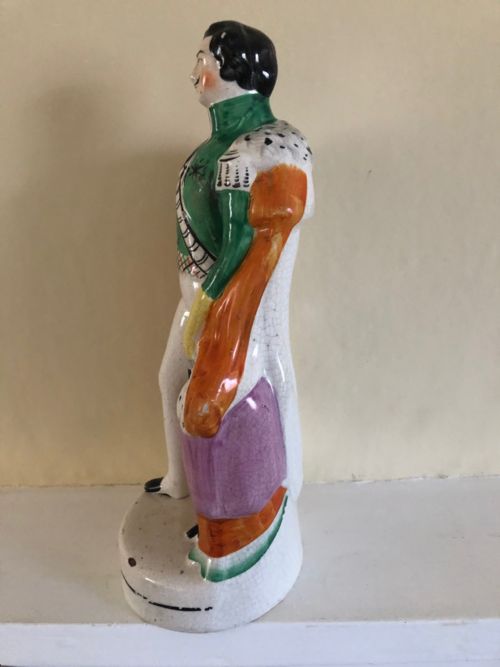 fig 3. A Victorian Staffordshire earthenware figure depicting Prince Albert standing in a green tunic and orange cloak on a rounded pedestal base.