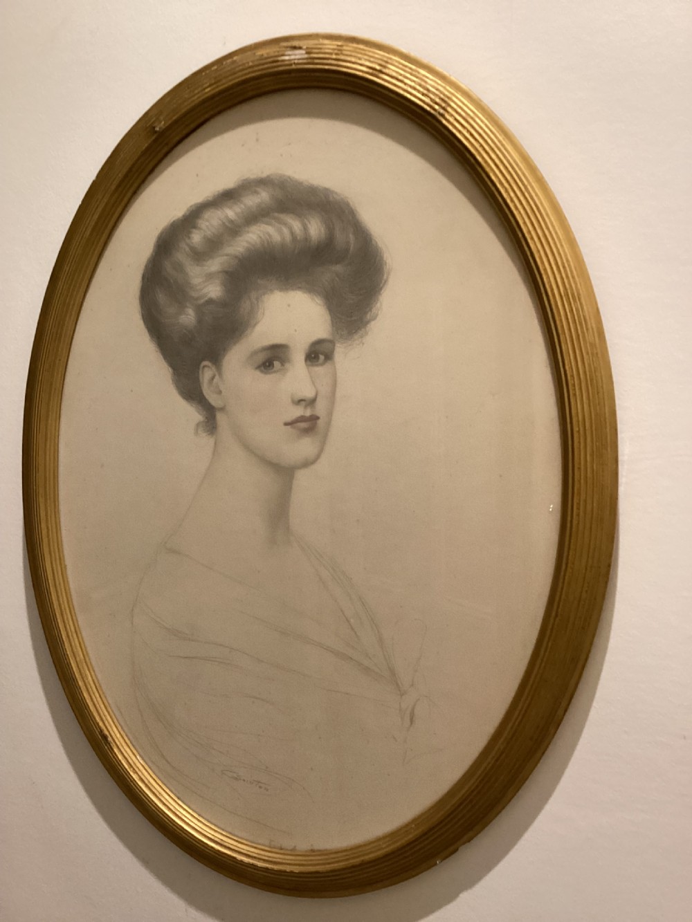 An oval gilt-framed drawing showing a profile-three-quarter portrait of an Edwardian woman with swept-up hair rendered in pencil and delicate wash.