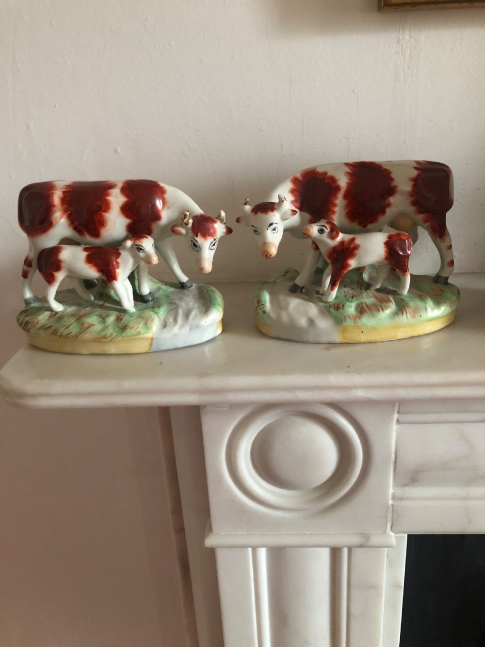 A pair of nineteenth-century earthenware Staffordshire figures featuring red and white cows standing alongside their calves on oval green grass bases.