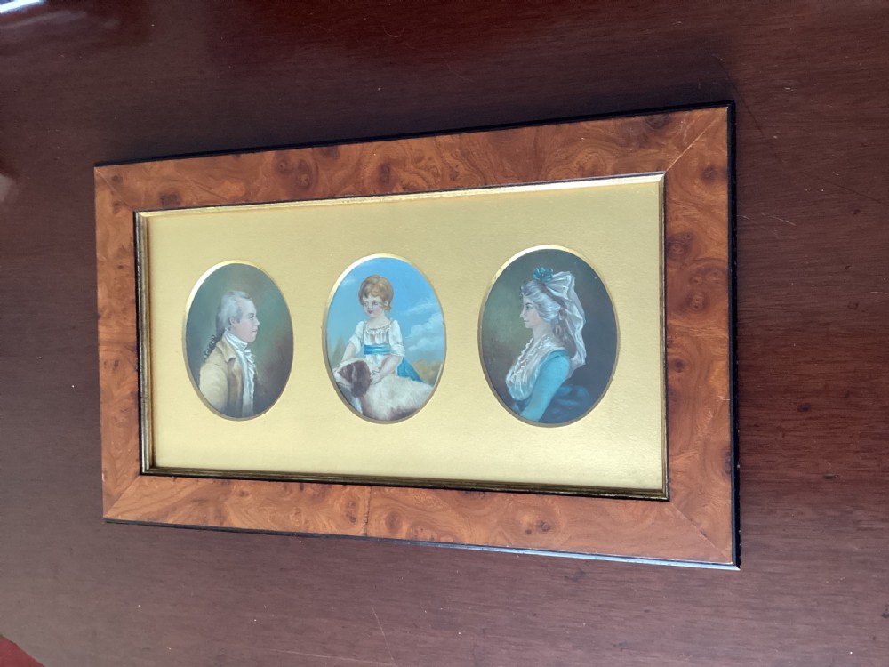 A rectangular burr wood frame enclosing three oval portrait miniatures of a man, a child with a dog, and a woman against a gold mount. View III