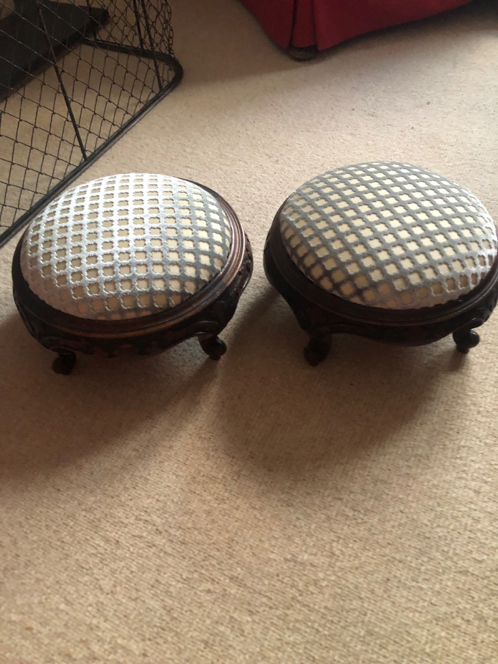 A pair of circular Victorian footstools featuring dark carved wooden frames with short cabriole legs and patterned grey and cream upholstered tops.