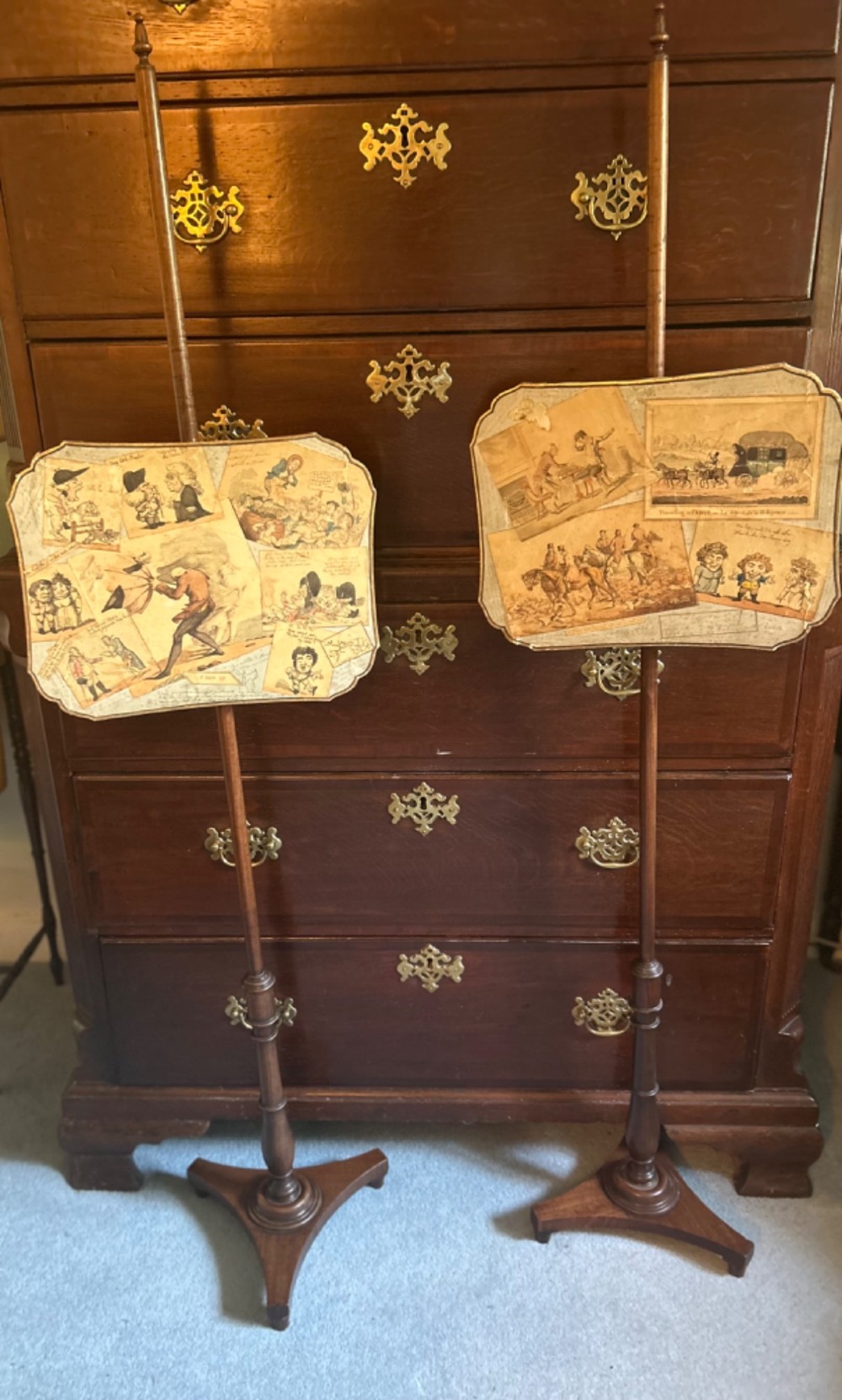 A pair of late George III mahogany pole screens featuring adjustable scalloped panels mounted with printed satirical caricatures on turned wooden stands with tripod bases.