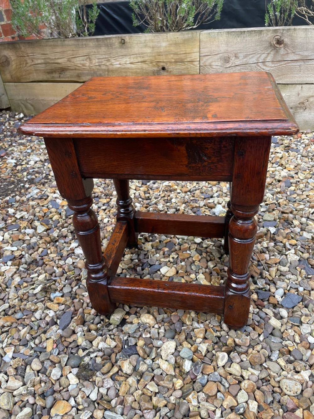 A dark oak joint stool featuring baluster turned legs, lower perimeter stretchers, and wooden peg construction.