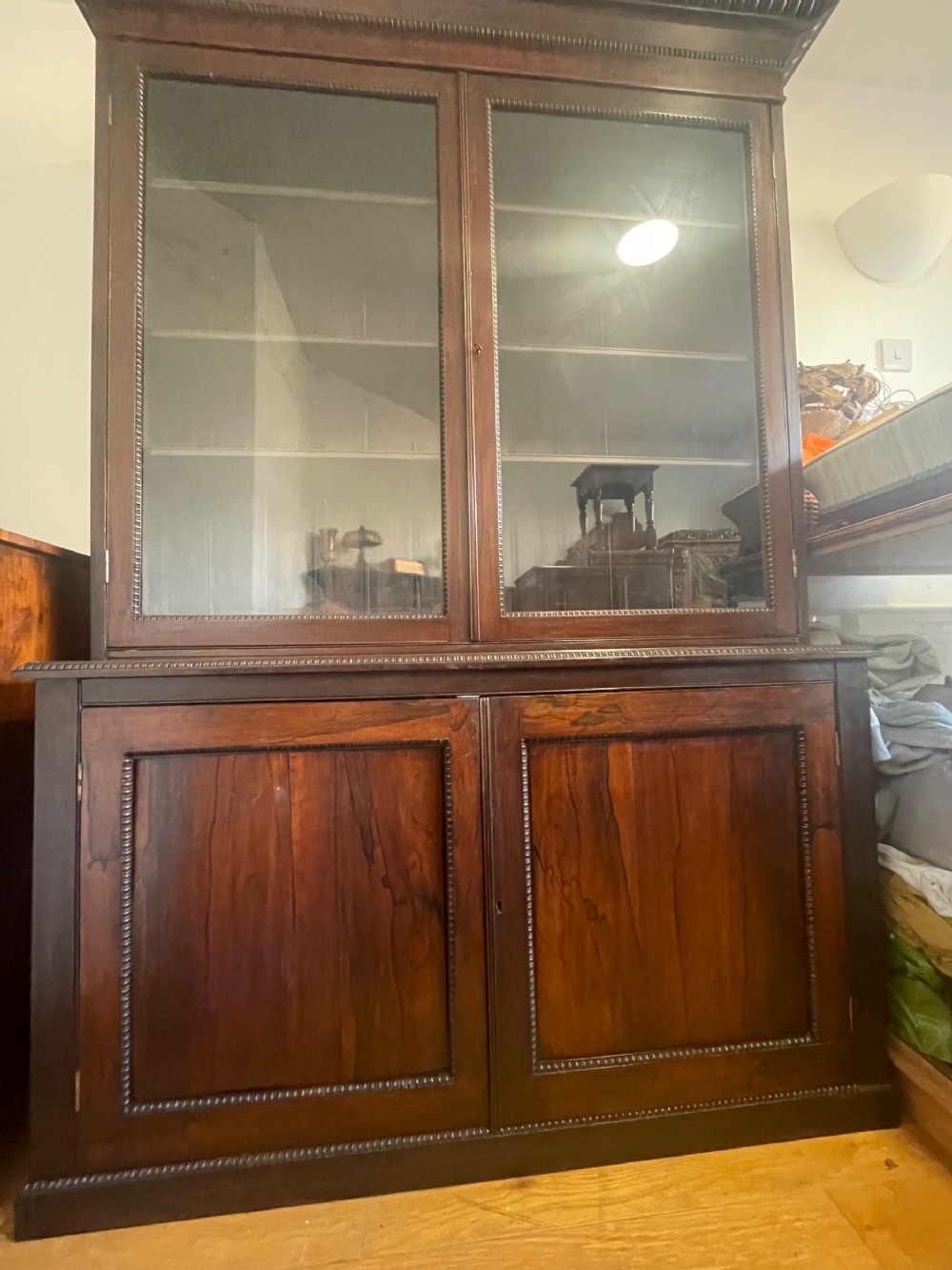 An antique Regency rosewood bookcase featuring an upper section with two glazed glass doors and a lower section with two solid panelled cabinet doors decorated with beaded moulding.