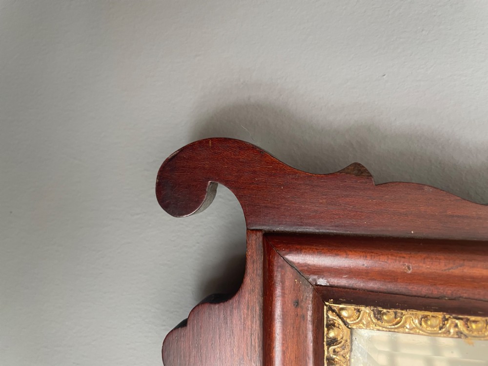 A dark mahogany Chippendale style wall mirror featuring fret-cut scrollwork cresting with a starburst inlay and a gilded inner border. View IV