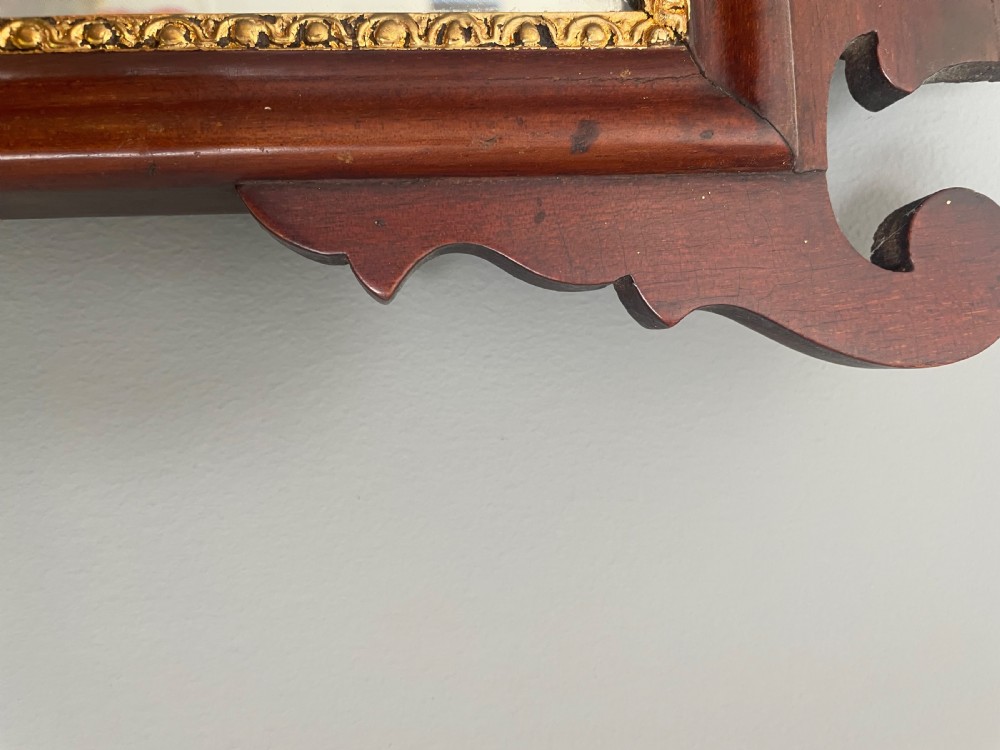 A dark mahogany Chippendale style wall mirror featuring fret-cut scrollwork cresting with a starburst inlay and a gilded inner border. View V