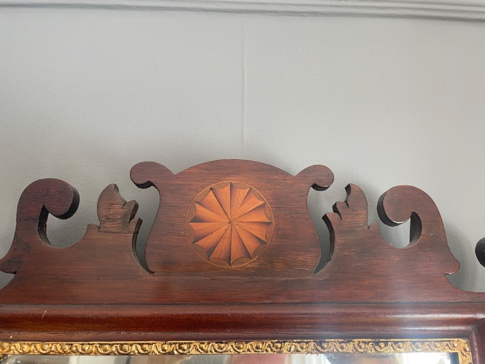 A dark mahogany Chippendale style wall mirror featuring fret-cut scrollwork cresting with a starburst inlay and a gilded inner border. View VI