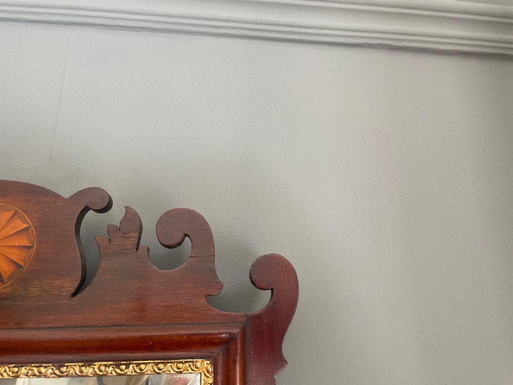 A dark mahogany Chippendale style wall mirror featuring fret-cut scrollwork cresting with a starburst inlay and a gilded inner border. View VII
