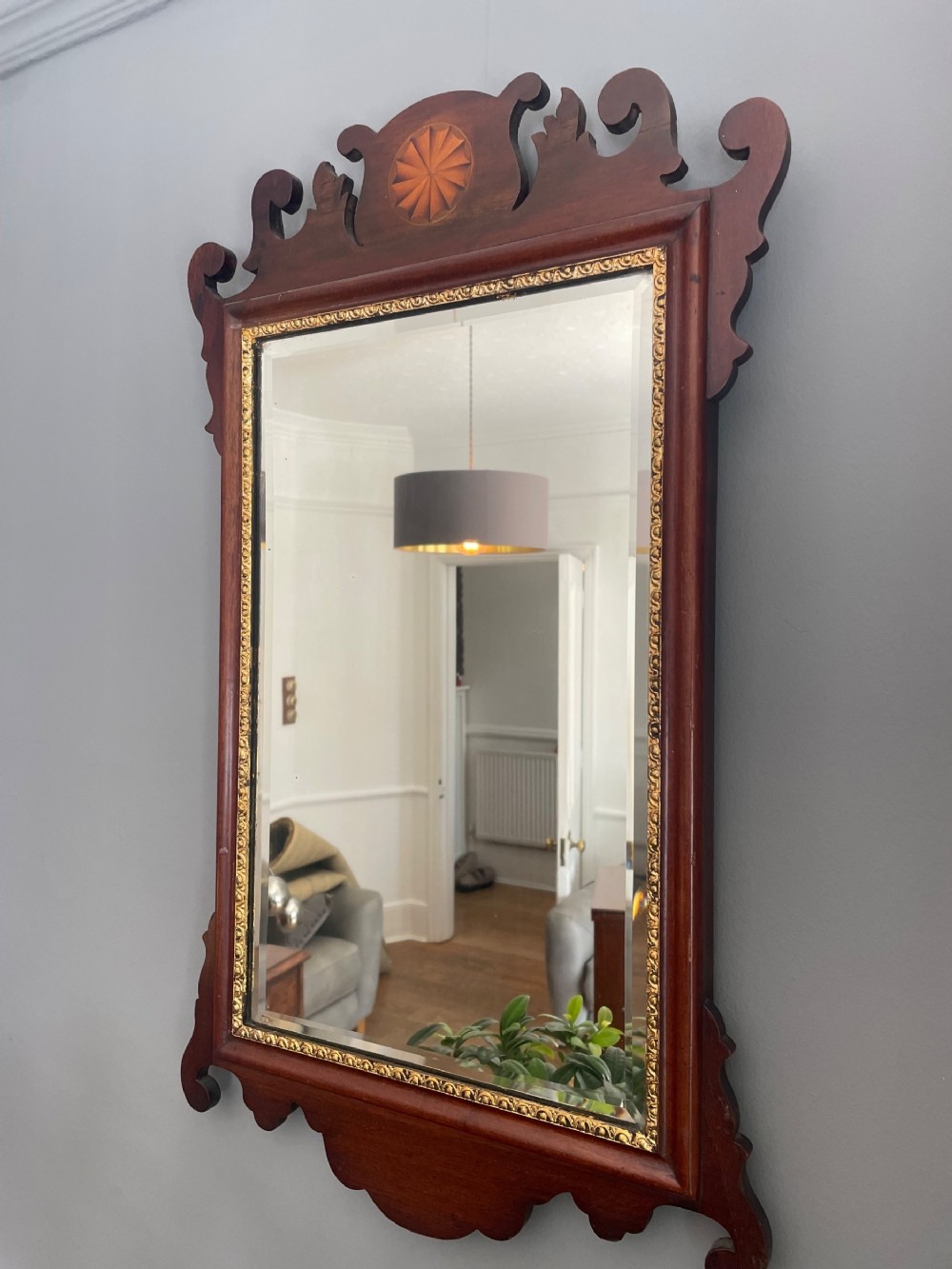 A dark mahogany Chippendale style wall mirror featuring fret-cut scrollwork cresting with a starburst inlay and a gilded inner border.