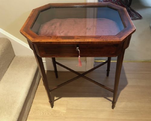 fig 1. An Edwardian mahogany bijouterie table featuring a canted octagonal glazed top, satinwood stringing inlay, and slender tapered legs with cross stretchers.