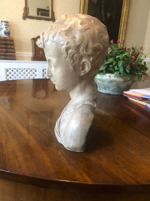 fig 1. A 19th-century terracotta-style sculptural bust depicting a youth with curled hair and draped garments looking downwards.