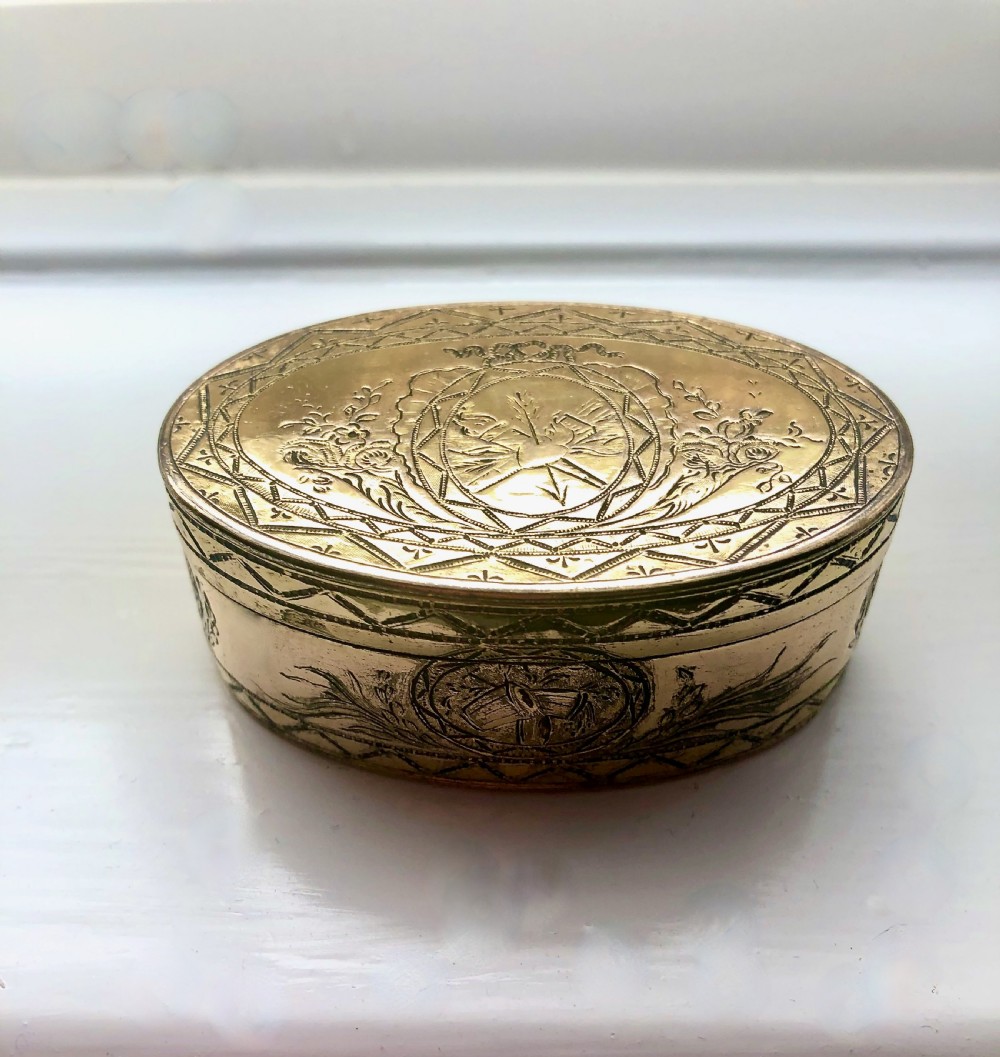 An oval Georgian gold-plated snuff box featuring detailed bright-cut engravings of floral garlands, arrows, and geometric borders.