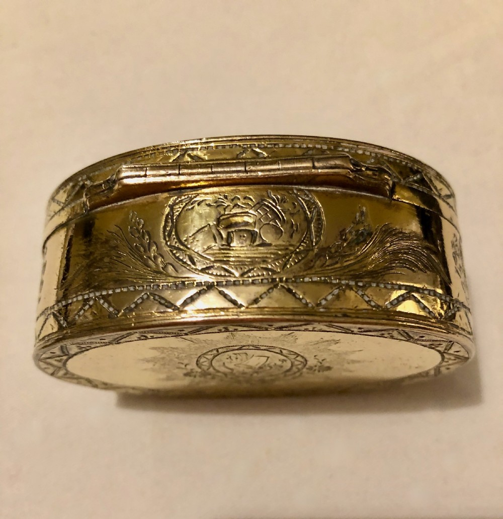 An oval Georgian gold-plated snuff box featuring detailed bright-cut engravings of floral garlands, arrows, and geometric borders. View II