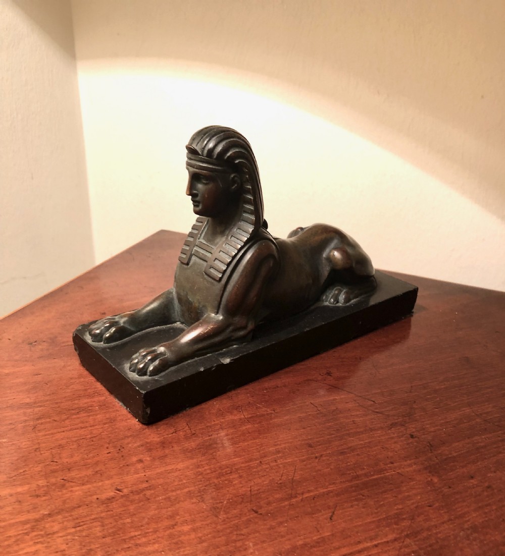 A late 19th-century dark bronze sculpture depicting a couchant sphinx wearing a nemes headdress, mounted on a rectangular black base. View II