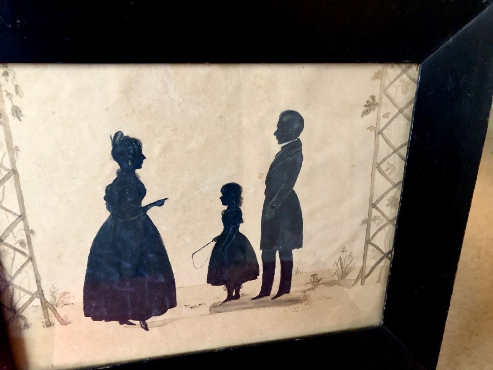 A late 19th-century framed British silhouette depicting a mother, child, and father in profile against an off-white background with trellised details. View V