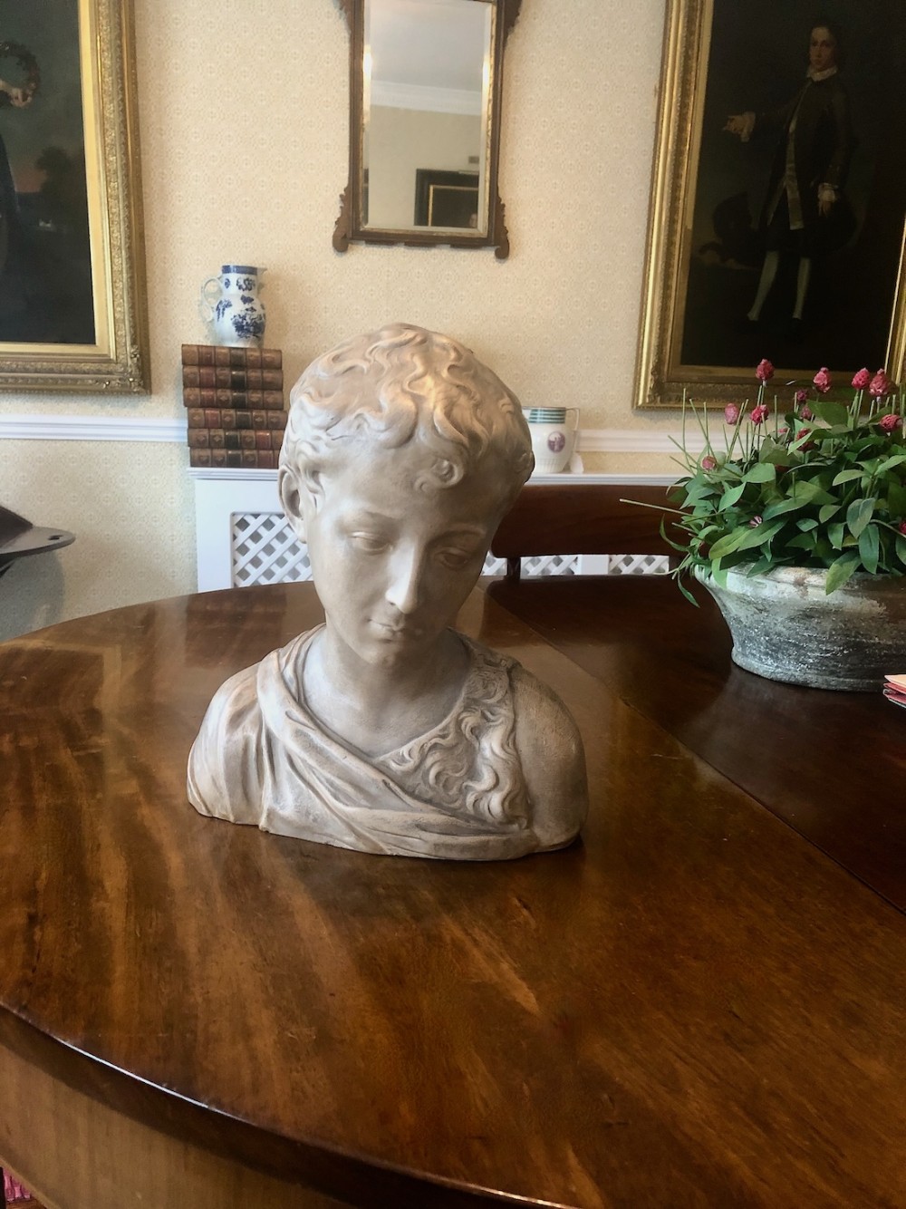 A 19th-century terracotta-style sculptural bust depicting a youth with curled hair and draped garments looking downwards.