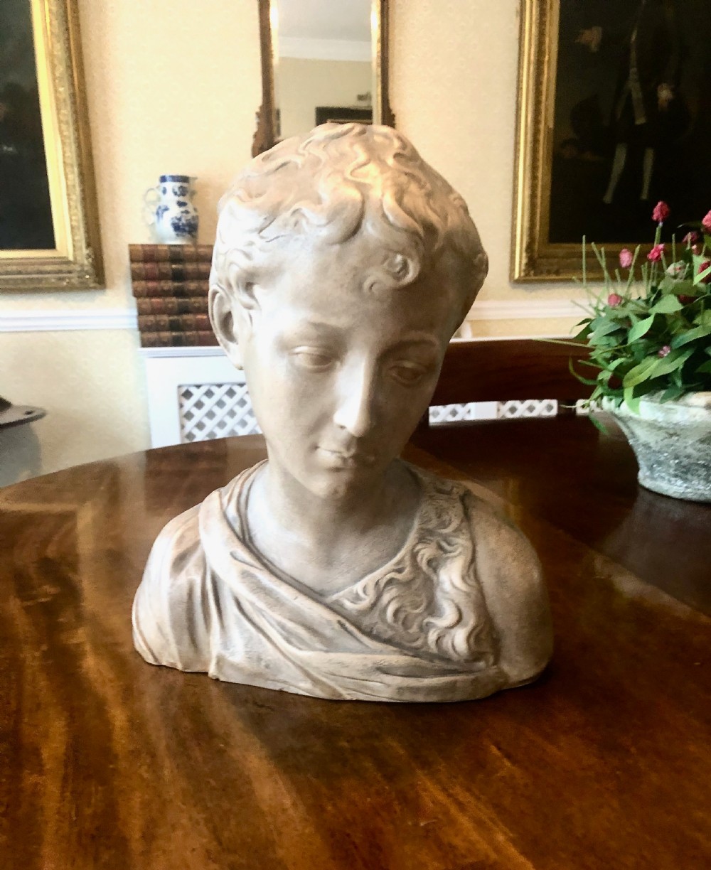 A 19th-century terracotta-style sculptural bust depicting a youth with curled hair and draped garments looking downwards. View III