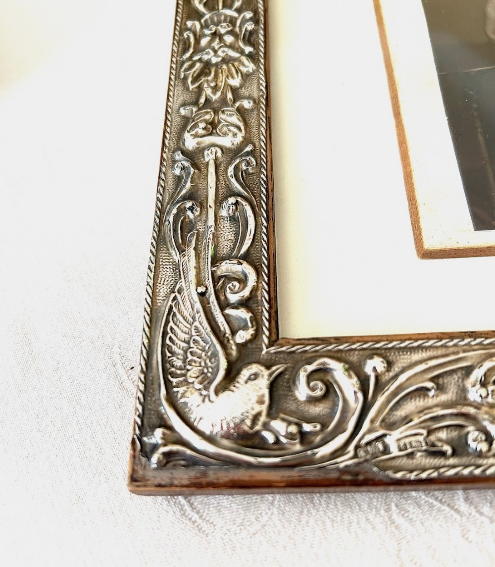 A rectangular Edwardian sterling silver picture frame featuring elaborate embossed scrollwork, foliate patterns, and mythical motifs surrounding a central portrait print. View V