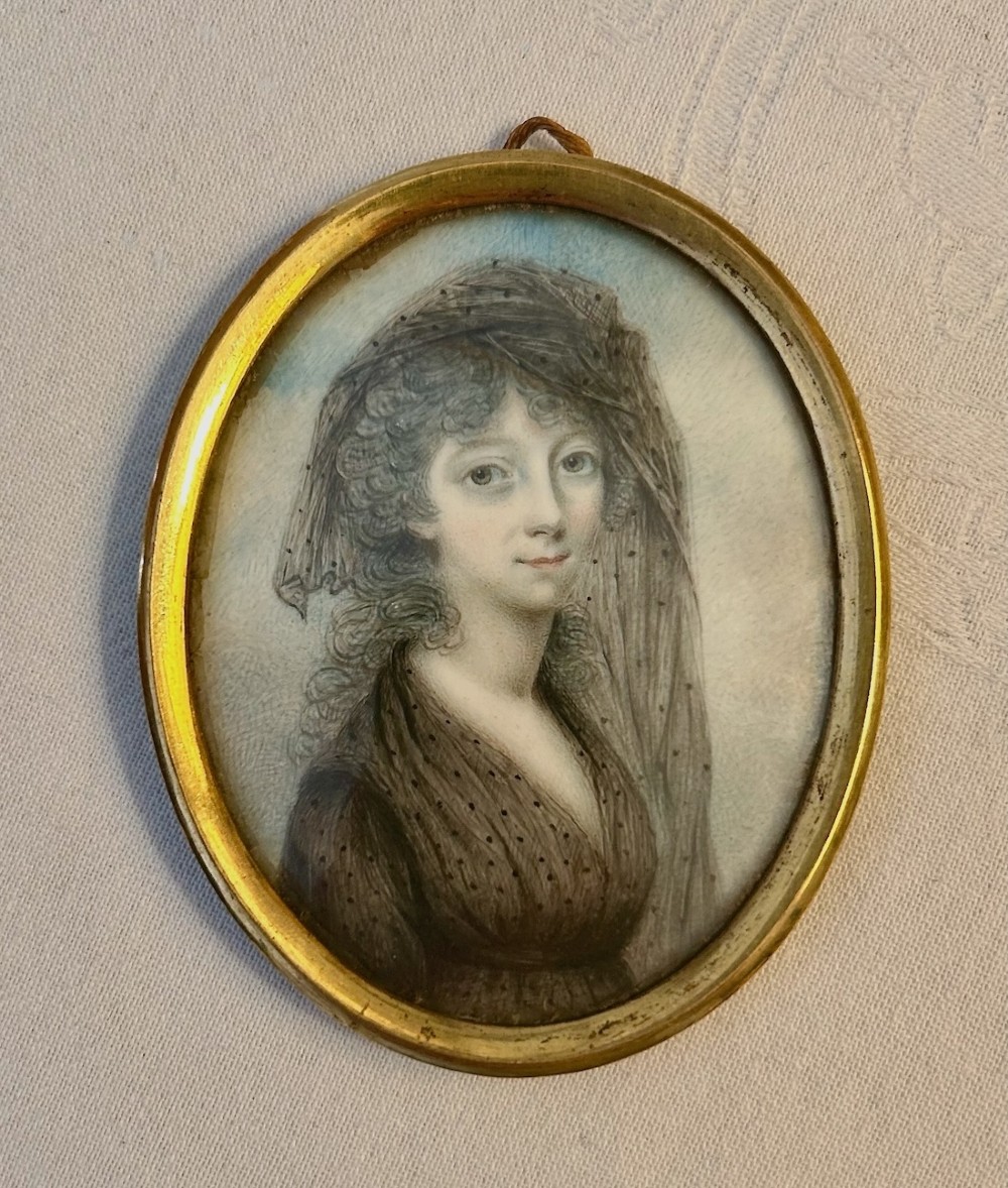 An oval Georgian portrait miniature depicting a woman wearing a laced veil set inside a narrow gilt metal frame with a suspension loop. View II
