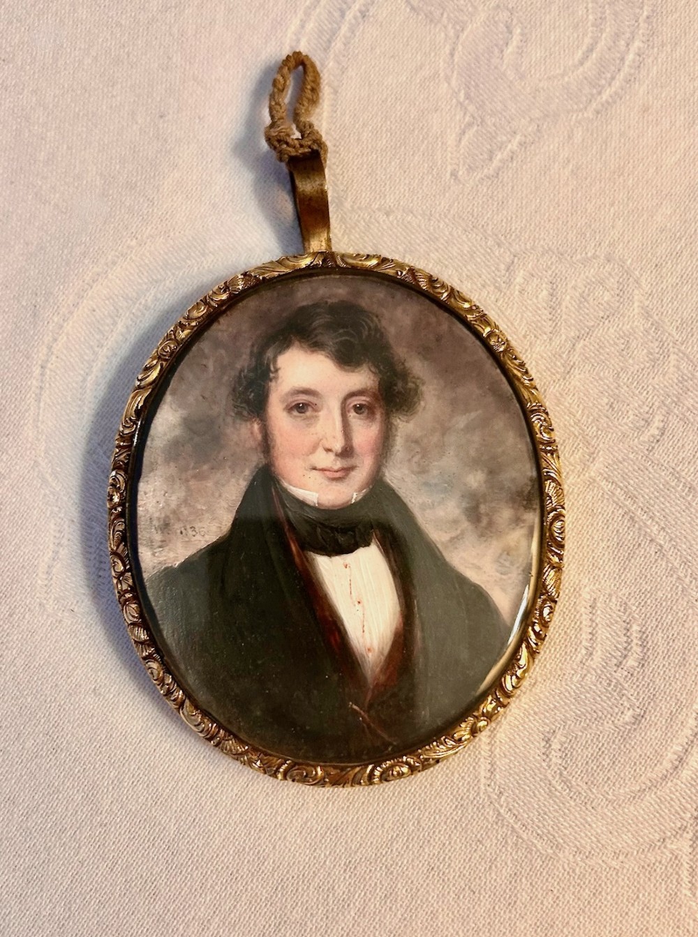 An oval Georgian portrait miniature painting depicting a gentleman with dark hair and a white cravat, housed in a chased gilt-metal frame with a top suspension loop. View III