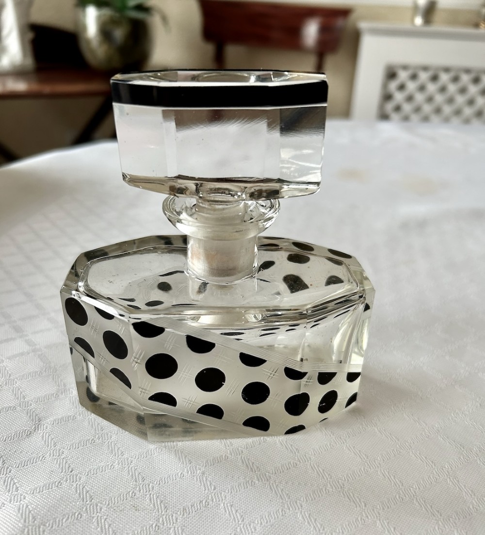 An Art Deco clear glass scent bottle featuring black polka dots across a diagonal band with a faceted geometric cut stopper.