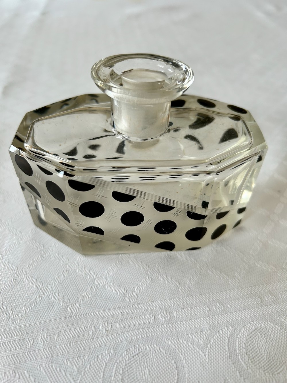 An Art Deco clear glass scent bottle featuring black polka dots across a diagonal band with a faceted geometric cut stopper. View IV