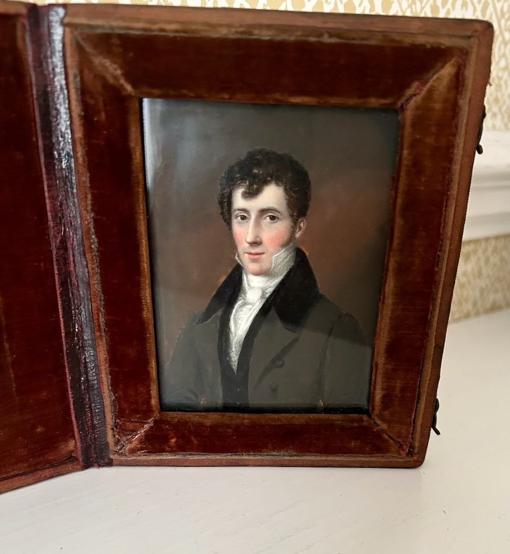An early Victorian portrait miniature painting depicting a gentleman in a dark coat, housed within a red velvet-lined folding case.