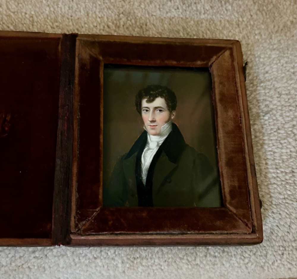 An early Victorian portrait miniature painting depicting a gentleman in a dark coat, housed within a red velvet-lined folding case. View V