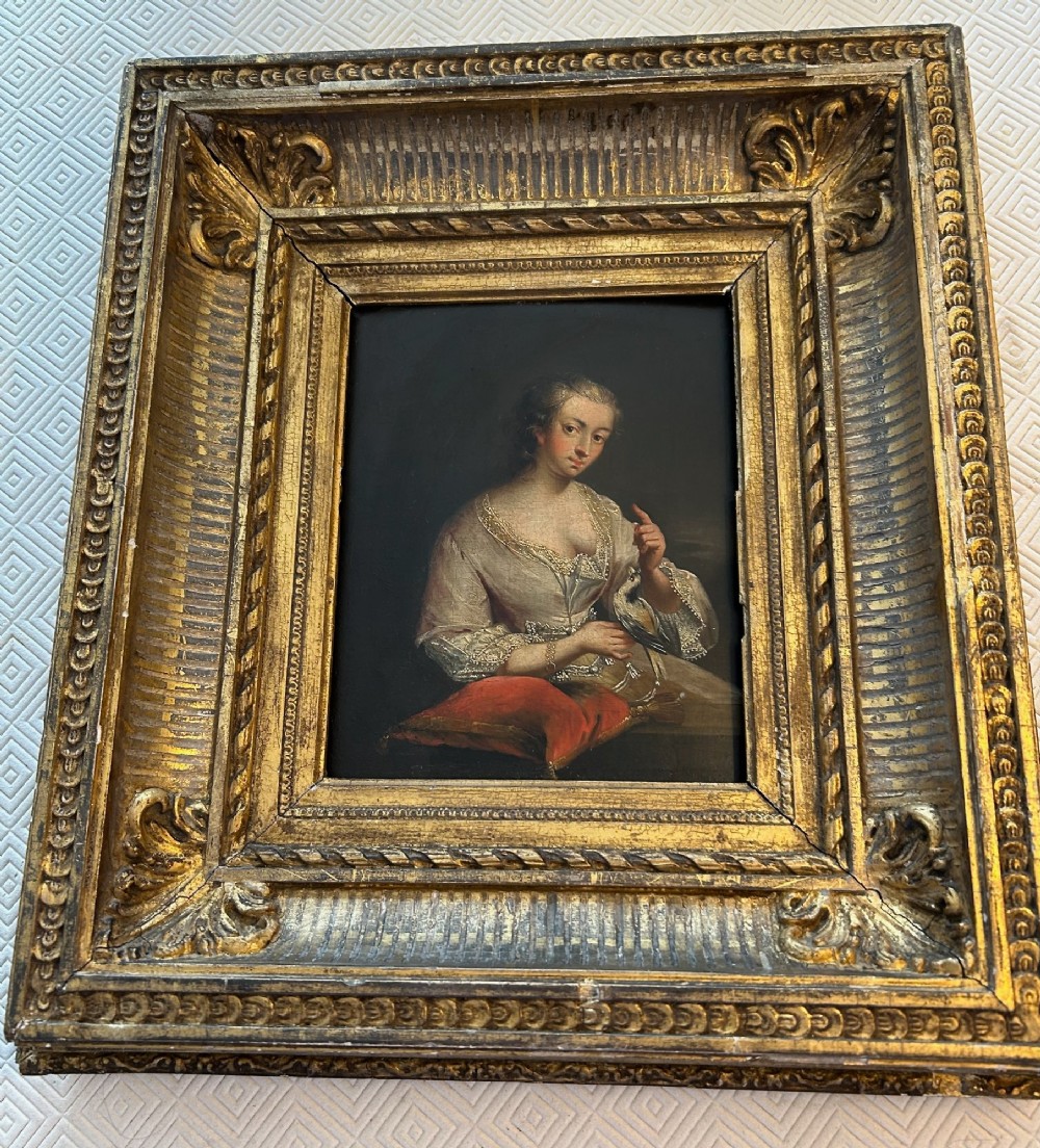An antique oil portrait depicting a woman in 18th-century dress holding a small bird, set within a deeply moulded gold giltwood frame.