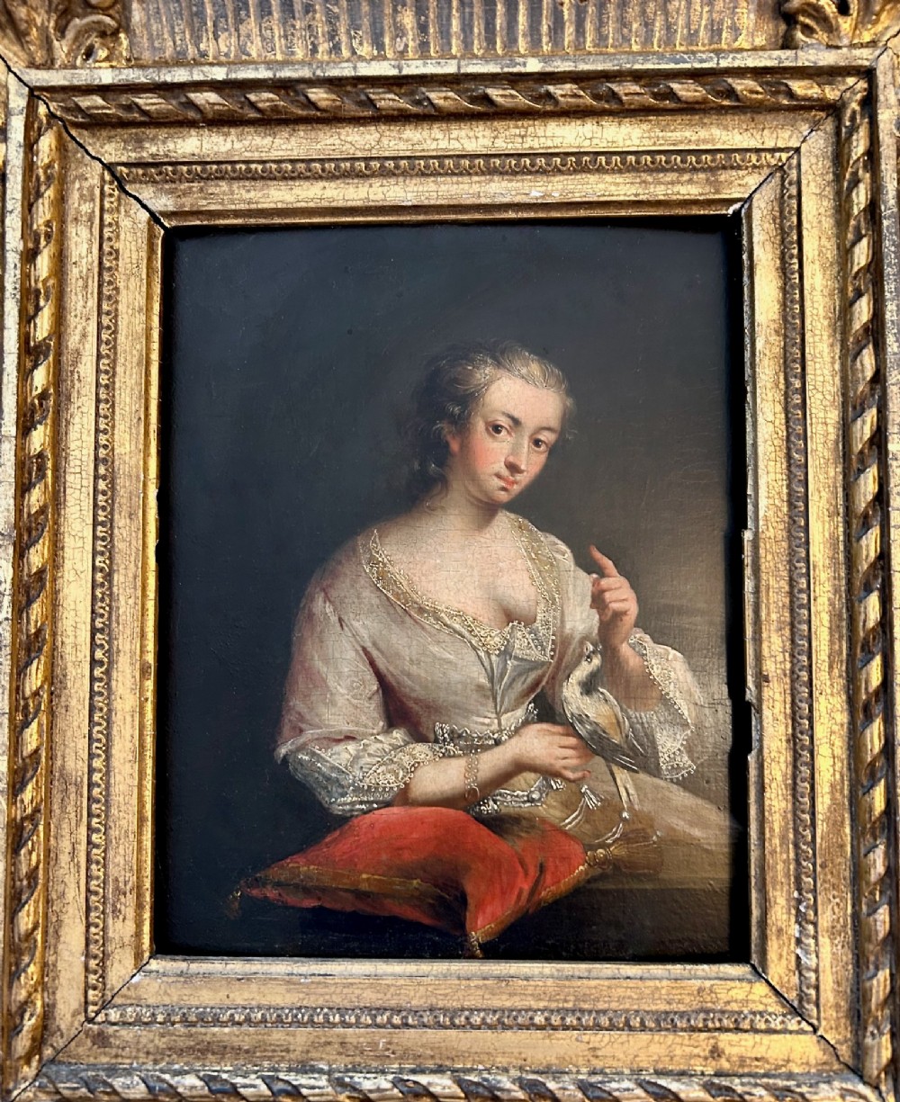 An antique oil portrait depicting a woman in 18th-century dress holding a small bird, set within a deeply moulded gold giltwood frame. View II