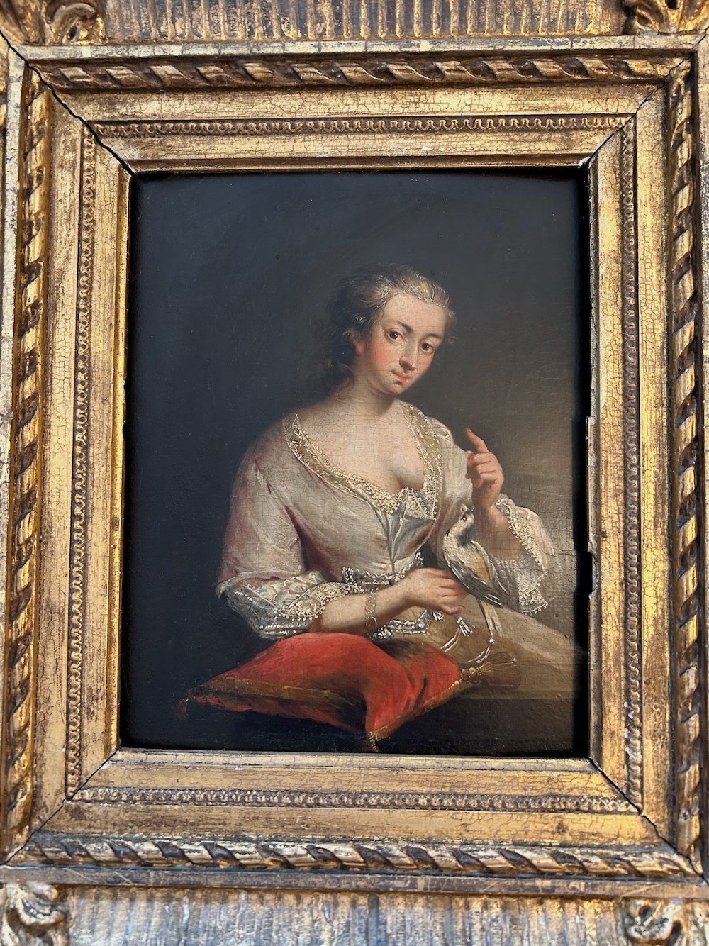 An antique oil portrait depicting a woman in 18th-century dress holding a small bird, set within a deeply moulded gold giltwood frame. View III