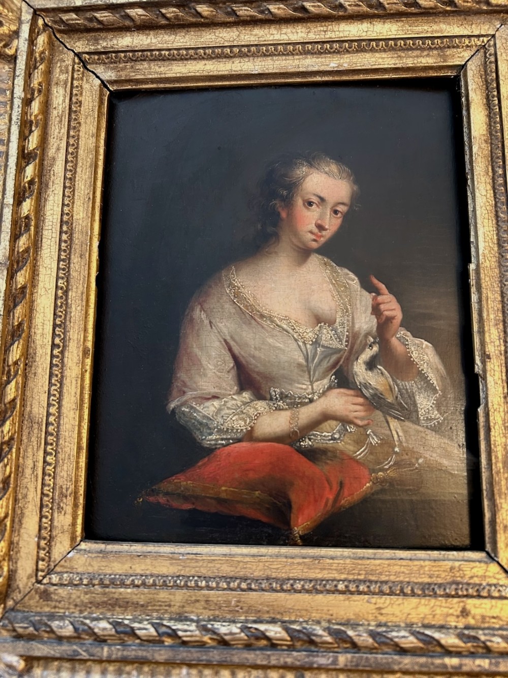 An antique oil portrait depicting a woman in 18th-century dress holding a small bird, set within a deeply moulded gold giltwood frame. View IV