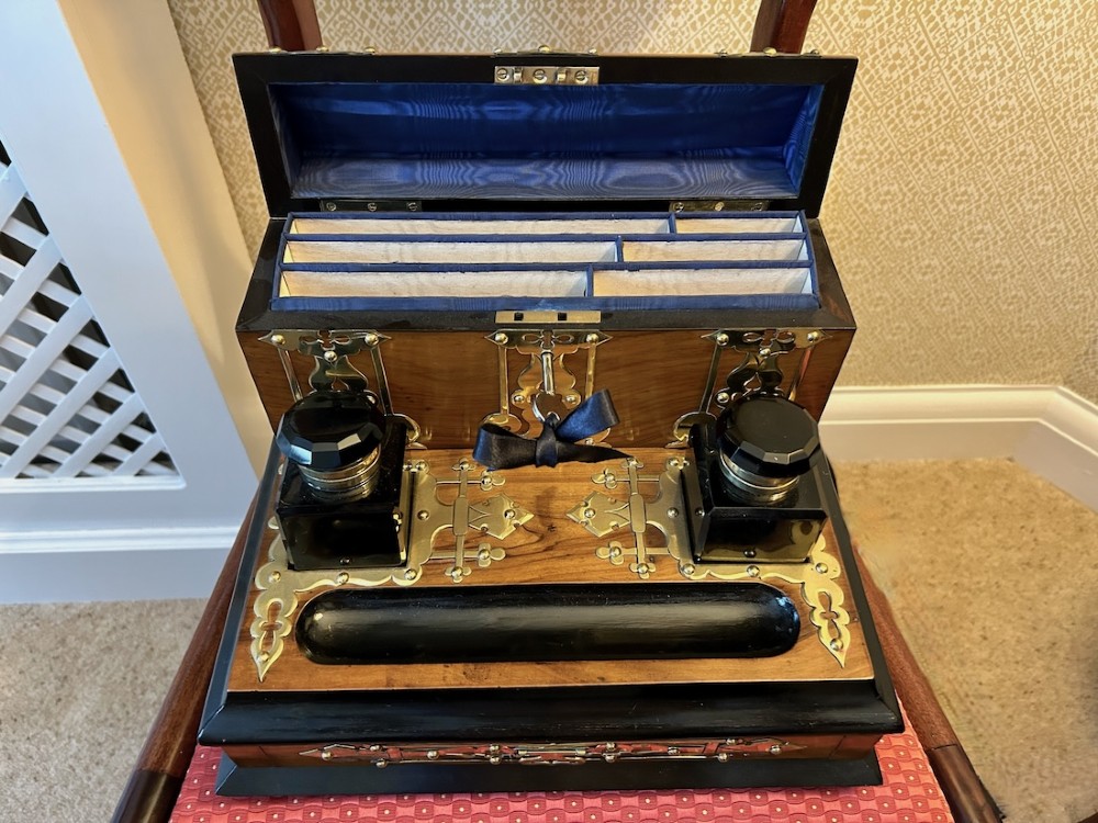 An open Victorian figured walnut desk stand featuring decorative brass strapwork, two black inkwells, a pen trough, and an upper stationery compartment lined in blue fabric.