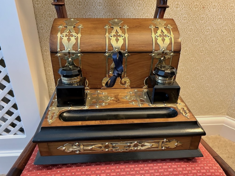 An open Victorian figured walnut desk stand featuring decorative brass strapwork, two black inkwells, a pen trough, and an upper stationery compartment lined in blue fabric. View II