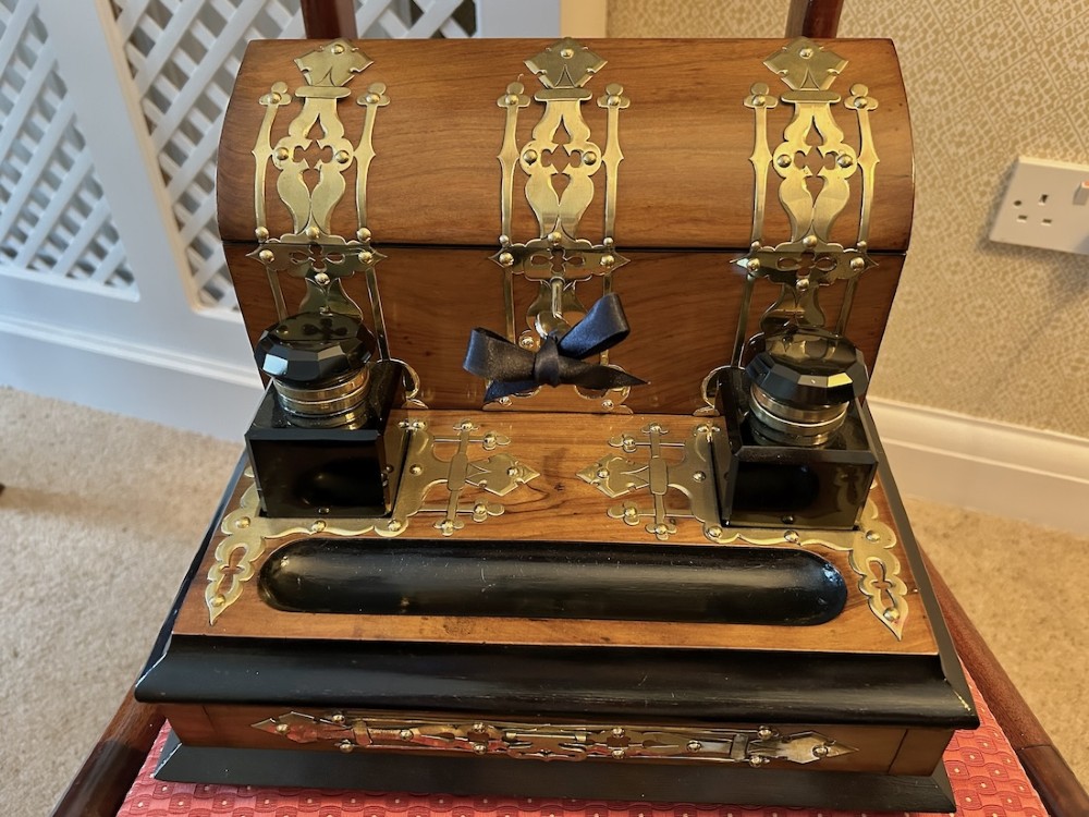 An open Victorian figured walnut desk stand featuring decorative brass strapwork, two black inkwells, a pen trough, and an upper stationery compartment lined in blue fabric. View VI
