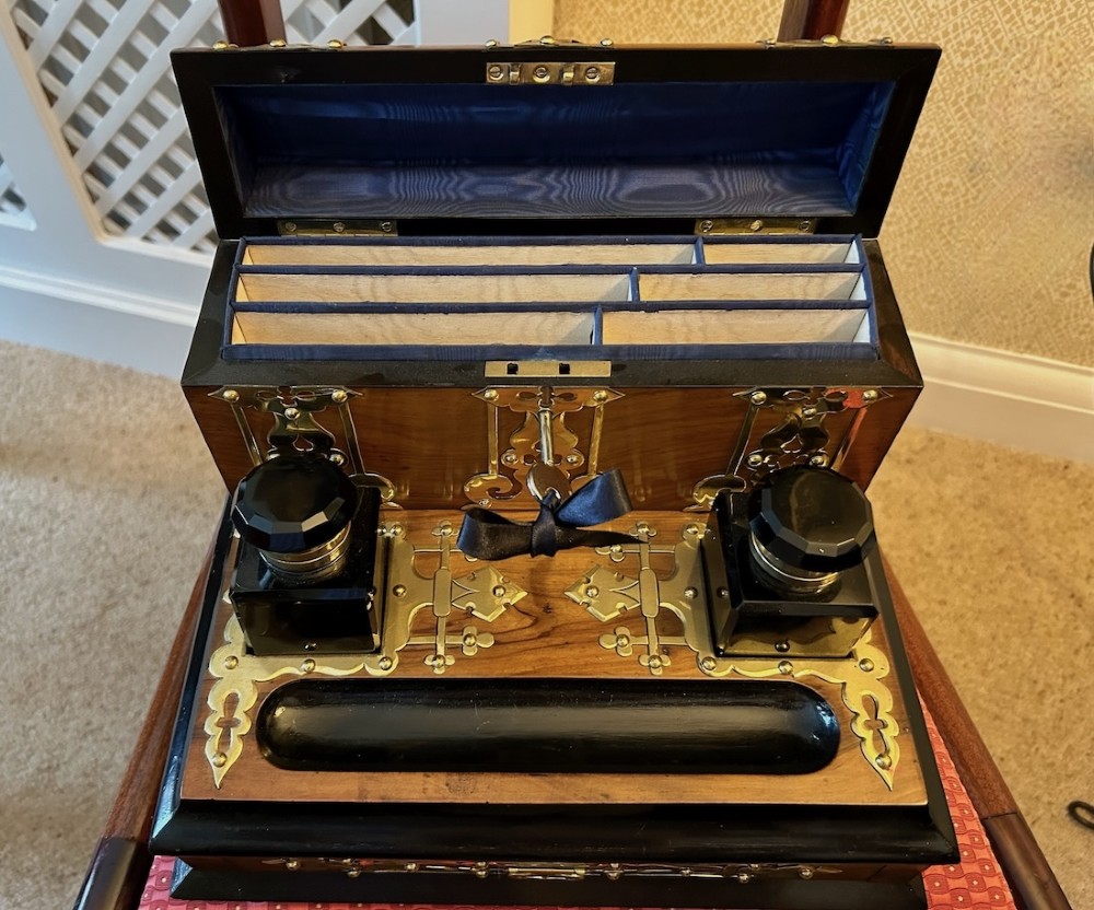 An open Victorian figured walnut desk stand featuring decorative brass strapwork, two black inkwells, a pen trough, and an upper stationery compartment lined in blue fabric. View VII