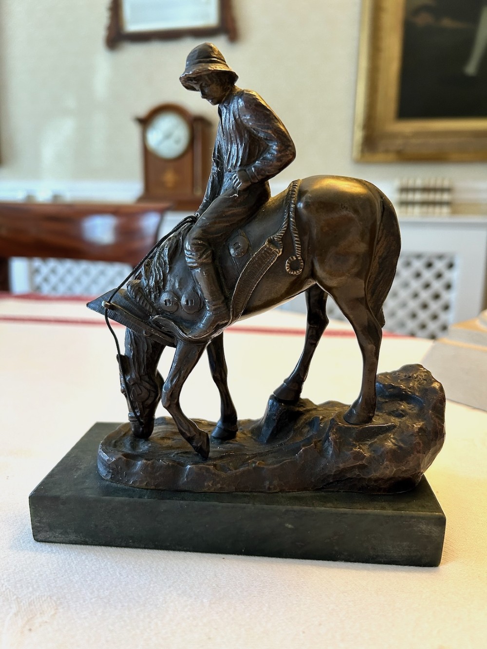 A cast bronze sculpture depicting a young boy wearing a hat seated upon a grazing horse, mounted on a dark rectangular marble base. View II