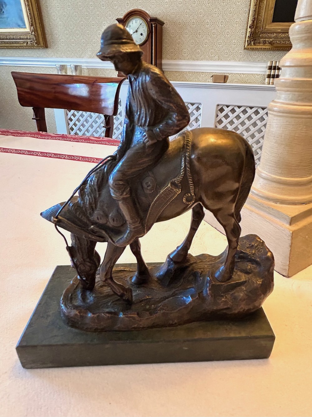 A cast bronze sculpture depicting a young boy wearing a hat seated upon a grazing horse, mounted on a dark rectangular marble base. View V