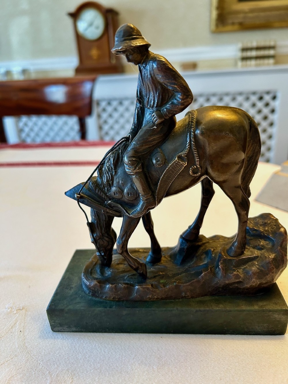 A cast bronze sculpture depicting a young boy wearing a hat seated upon a grazing horse, mounted on a dark rectangular marble base. View VI