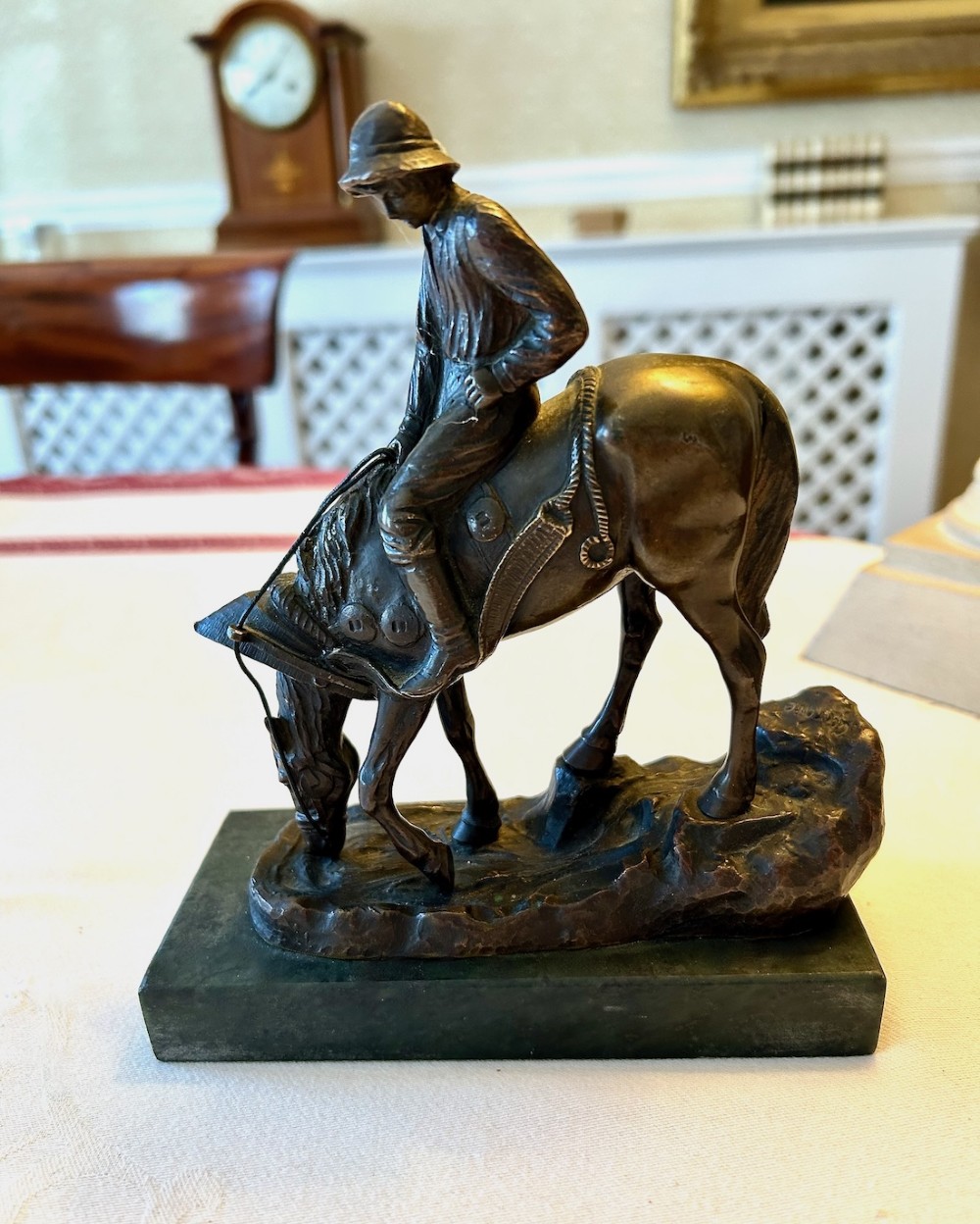 A cast bronze sculpture depicting a young boy wearing a hat seated upon a grazing horse, mounted on a dark rectangular marble base. View VII