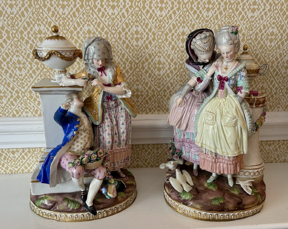 A pair of 19th-century hand-painted Meissen porcelain figurines depicting figures in 18th-century court dress alongside classical urns. View X