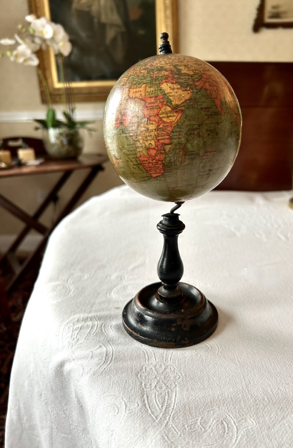 A small 1920s Geographia terrestrial globe featuring printed paper gores set upon a dark turned wooden pedestal stand.