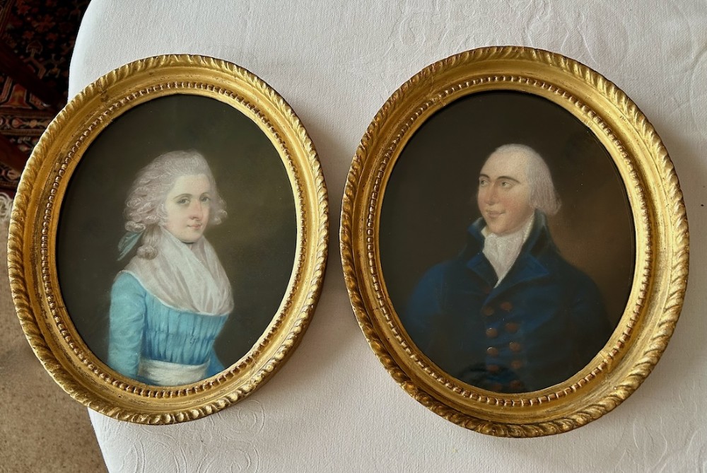 A pair of 18th-century oval pastel portraits depicting a woman in a blue dress and a man in a blue coat, housed in matching giltwood frames.