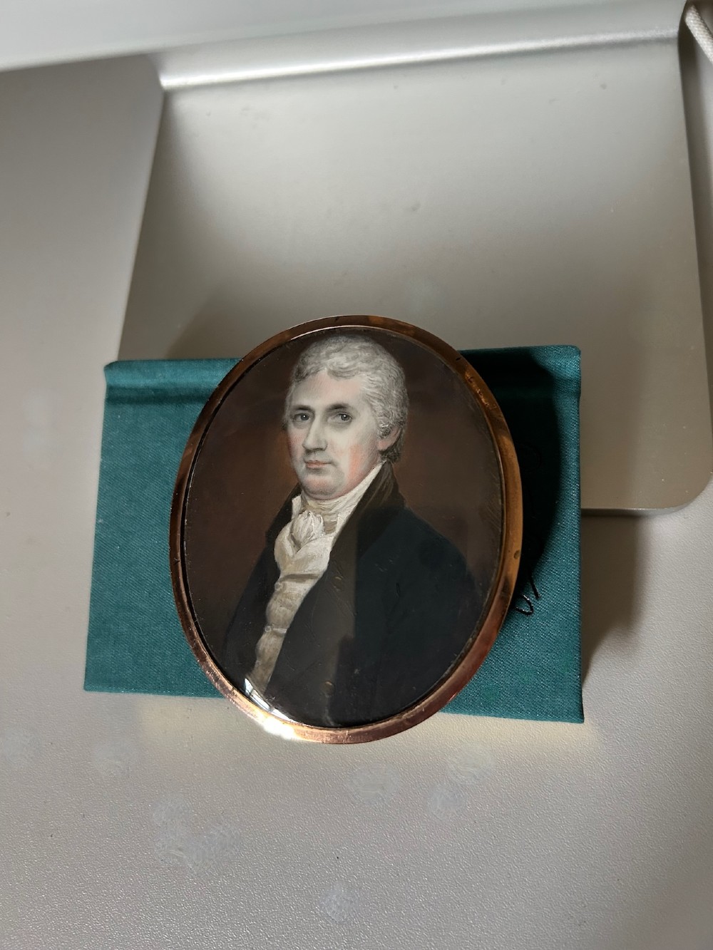 An oval Georgian portrait miniature depicting a gentleman with grey hair wearing a dark coat and white cravat, housed within a gold-plated frame. View III