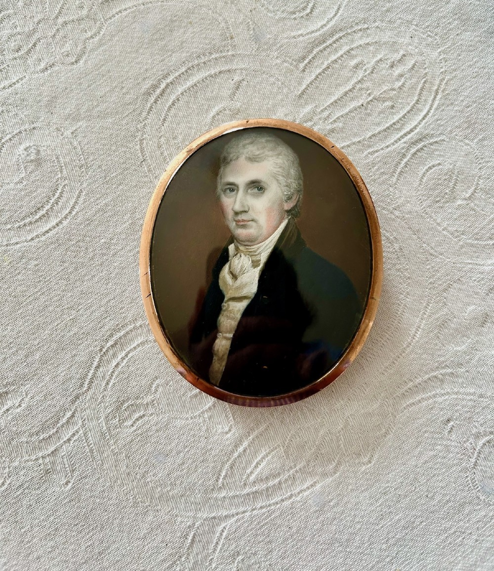 An oval Georgian portrait miniature depicting a gentleman with grey hair wearing a dark coat and white cravat, housed within a gold-plated frame. View IV