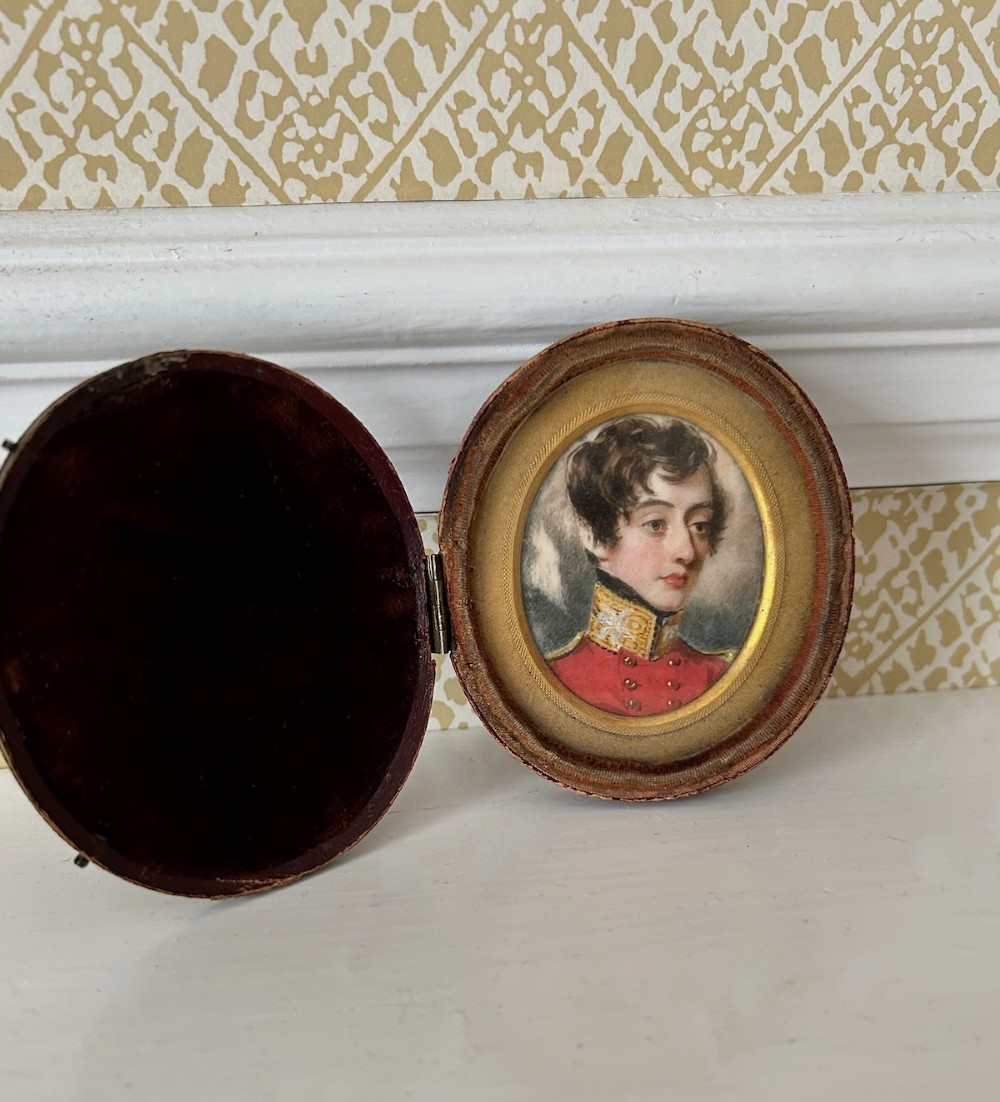An oval antique portrait miniature depicting a young officer in a scarlet uniform, presented inside an open red leather case. View V