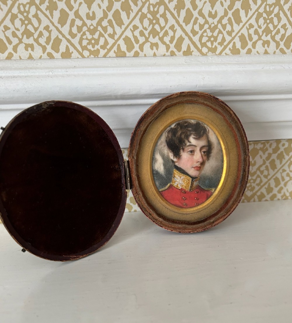 An oval antique portrait miniature depicting a young officer in a scarlet uniform, presented inside an open red leather case. View VI