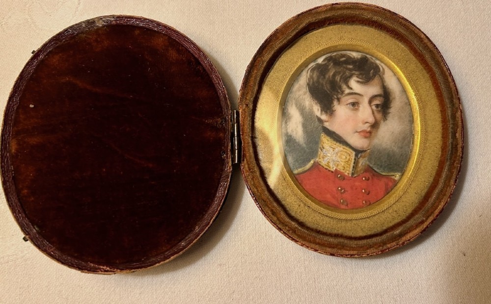An oval antique portrait miniature depicting a young officer in a scarlet uniform, presented inside an open red leather case. View VII