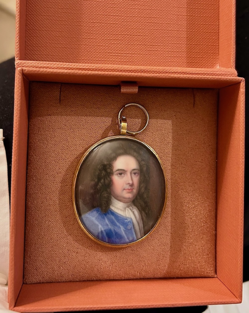 An oval Georgian portrait miniature set in a gold-tone metal frame depicting a gentleman with a long dark wig, white cravat, and blue coat. View II