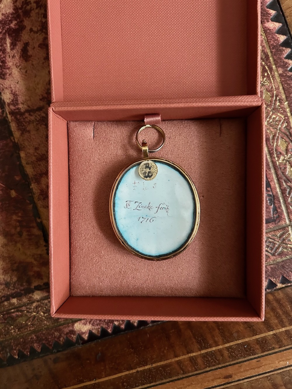 An oval Georgian portrait miniature set in a gold-tone metal frame depicting a gentleman with a long dark wig, white cravat, and blue coat. View V